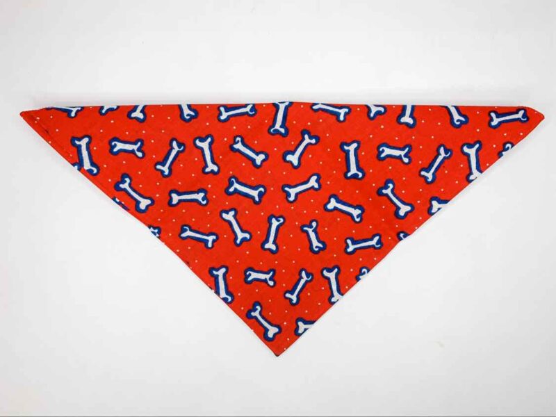 Tossed Bones Red Triangle Bandana - 22x29x22 Inch A red triangular bandana features a repeating pattern of white dog bones outlined in blue set against a dotted background typically used as a pet accessory or decorative item.