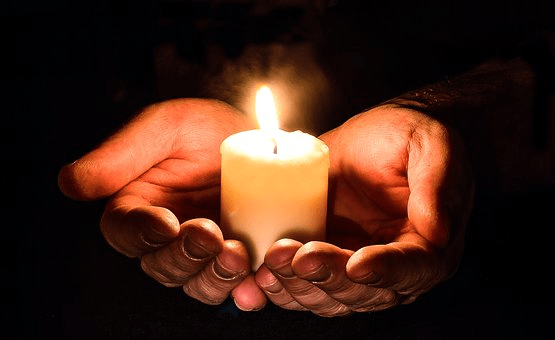 A candle in the dark held by both hands.