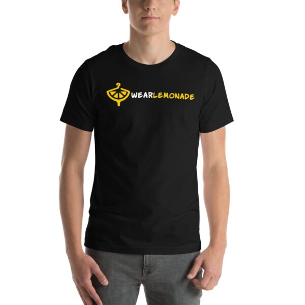 A person stands wearing a black t-shirt featuring a lemon logo and the text WE ARE LEMONADE in yellow and white on the front in a neutral setting.