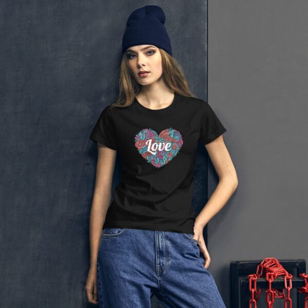 A young woman wearing a black t-shirt with a colorful heart design featuring the word love stands against a textured wall with a modern industrial background and red chains.