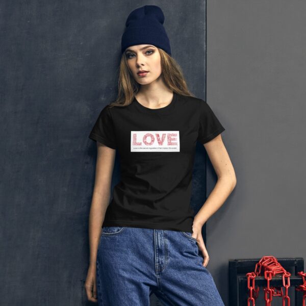 A woman is standing confidently wearing a black t-shirt that features the word LOVE. She is looking directly at the viewer against a textured gray backdrop with some red chains in the corner.