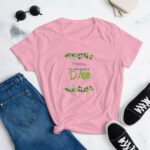 A pink T-shirt with the text Happy ST. PATRICK'S DAY surrounded by green shamrocks is displayed next to rolled-up denim jeans and black sneakers on a light background.
