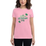 A woman stands smiling while wearing a pink t-shirt featuring the text "Happy St. Patrick's Day" in green with decorative elements  set against a neutral background.