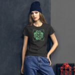 A young woman stands against a textured gray wall wearing a dark t-shirt with a green shamrock design and text that reads "Happy St. Patrick's Day" paired with baggy jeans and a beanie.