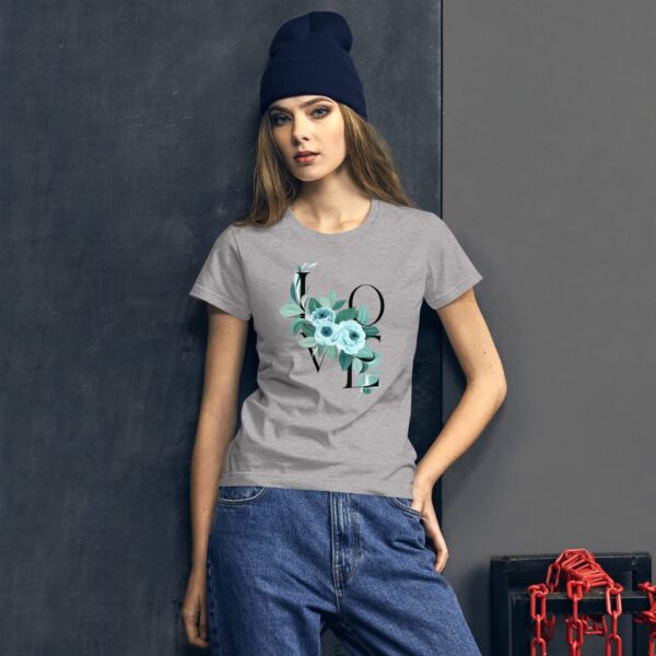 A young woman is posing while wearing a gray t-shirt with a floral design spelling "LOVE" in black. She has long hair and is wearing a dark beanie. The background is dark  featuring a black surface and red chains.