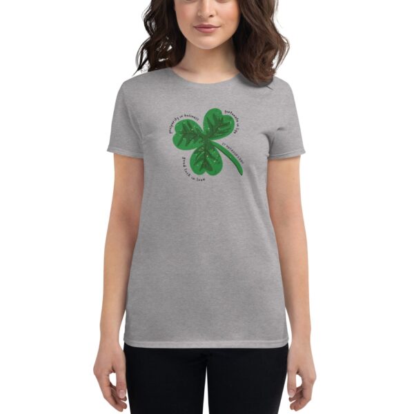 A person stands wearing a light gray t-shirt featuring a green four-leaf clover graphic. Surrounding the clover are circular phrases including "perfectly imperfect" and "lucky in love."