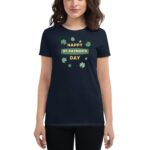 A dark t-shirt displays the words "HAPPY ST. PATRICK'S DAY" surrounded by green shamrocks  worn by a woman with wavy hair in a neutral setting.