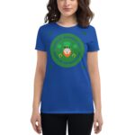 A woman wearing a blue t-shirt with a graphic design featuring a leprechaun and clovers celebrates St. Patrick's Day while smiling at the camera in a casual setting. Text reads "HAPPY ST. PATRICK'S DAY."
