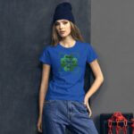 A woman wearing a blue t-shirt with a green shamrock design stands against a dark textured wall  exuding a casual yet festive vibe for St. Patrick's Day.