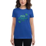 A woman wears a blue t-shirt featuring green text that says Happy St. Patrick's Day surrounded by symbols of celebration  standing in a neutral background.