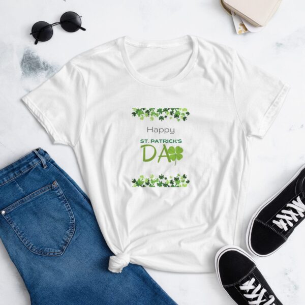 A white t-shirt featuring a festive design with green clovers and text that says Happy ST. PATRICK'S DAY is laid out next to blue jeans and black sneakers with white laces.