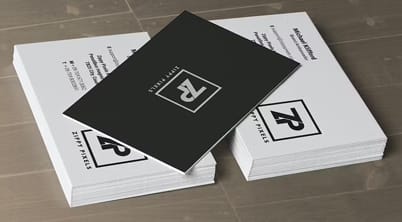 A stack of business cards is displayed on a surface with a black card on top featuring a white logo of the letter R surrounded by a geometric border.