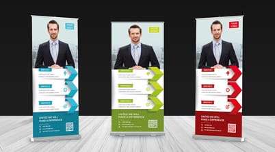 Three tall banner stands display a smiling man in formal attire with information below each image. The stands are colored blue green and red on a plain black background with wooden flooring.