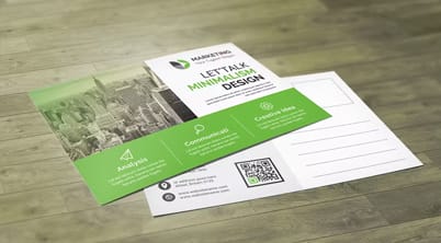 A green and white marketing brochure lies on a wooden surface showcasing the text LET'S TALK MINIMALISM DESIGN along with sections for analytics communication and contact ideas with a QR code present.