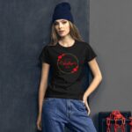 A woman stands against a textured dark wall wearing a black t-shirt with a red and gold design that says Happy Valentine’s Day alongside red heart graphics while wearing a blue beanie.