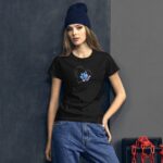 A young woman stands confidently against a textured dark wall wearing a black t-shirt with a colorful heart design and casual jeans complemented by a navy beanie.