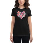 A woman wears a black t-shirt featuring a colorful floral heart design made of pink roses and green leaves in a simple indoor setting.