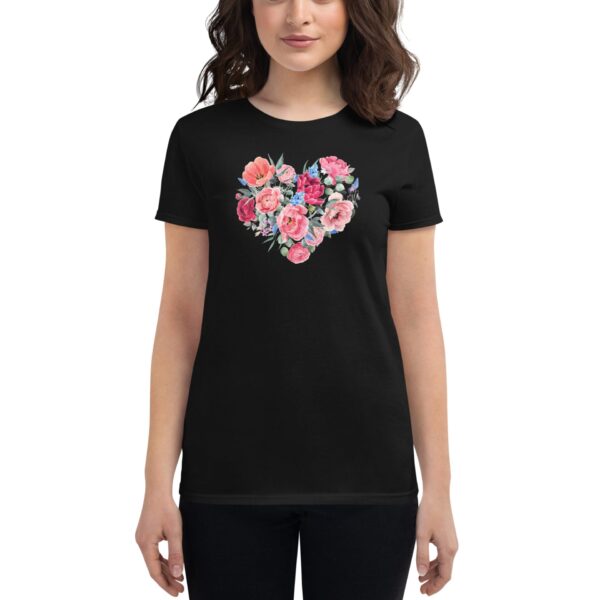 A woman wears a black t-shirt featuring a colorful floral heart design made of pink roses and green leaves in a simple indoor setting.
