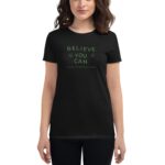 A woman is wearing a black t-shirt featuring the text "BELIEVE YOU CAN" and "HAPPY ST.PATRICK'S DAY" in green  set against a plain background.
