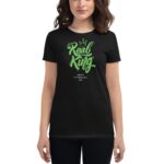 A woman is wearing a black t-shirt featuring the text "Real King" in green cursive with a crown design above it and the phrase "Happy St. Patrick's Day" below.
