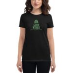 A person wears a black t-shirt featuring green text that reads GOOD VIBES and HAPPY ST.PATRICK'S DAY with a rainbow design above the text in a casual indoor setting.