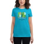 A woman stands wearing a bright turquoise t-shirt featuring colorful text that reads FOCUS ON THE Good Things with Happy St. Patricks 2024 below  smiling in a neutral background.