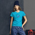 A young woman stands confidently wearing a bright turquoise t-shirt featuring a heart design with the word love and floral elements paired with dark high-waisted jeans in a stylish urban setting.