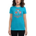 A woman wears a bright blue t-shirt featuring cartoon hearts with faces and flowers surrounded by text that says Happy Valentine's Day in playful font against a plain background.