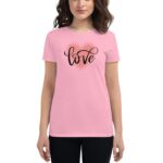 A woman wears a pink t-shirt featuring the word love in an elegant  scripted font on the front  while standing against a neutral background.