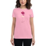 A woman wearing a pink t-shirt stands in front of the camera featuring an illustrated rose and the year 2024 beneath it  set against a neutral background.