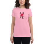 A woman wearing a pink shirt stands with a graphic design that spells "LOVE" featuring a red floral accent  presenting a casual yet stylish appearance in a neutral setting.