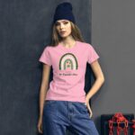 A model stands confidently wearing a pink t-shirt featuring a rainbow design with a shamrock and the text "HAPPY St. Patrick's Day" against a dark textured background.