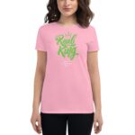 A woman wears a pink t-shirt featuring green text that says "Real King" along with "Happy St Patrick's Day" in a casual setting.