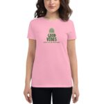 A young woman stands wearing a pink t-shirt featuring the text "GOOD VIBES" and "HAPPY ST.PATRICK'S DAY" in green letters  suggesting a festive atmosphere related to St. Patrick's Day.