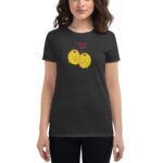 A woman wearing a dark shirt featuring two smiling yellow olives with the text OLIVE YOU is standing with her arms relaxed at her sides in a neutral setting.