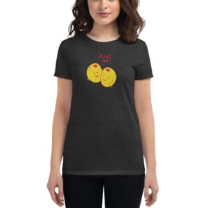 A woman wearing a dark shirt featuring two smiling yellow olives with the text OLIVE YOU is standing with her arms relaxed at her sides in a neutral setting.