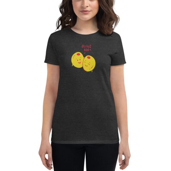 A woman wearing a dark shirt featuring two smiling yellow olives with the text OLIVE YOU is standing with her arms relaxed at her sides in a neutral setting.