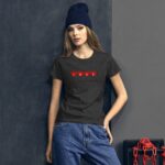 A young woman stands against a dark wall wearing a dark shirt with red hearts spelling "LOVE" while paired with casual blue jeans and a blue beanie  exuding a relaxed vibe.
