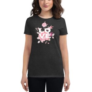 A woman stands wearing a dark gray t-shirt featuring the word "LOVE" surrounded by colorful floral designs  conveying a cheerful and stylish message in a casual indoor setting.