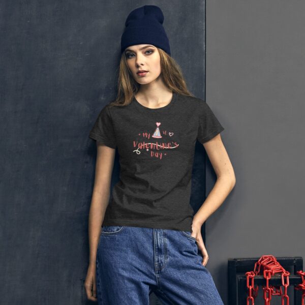 A young woman poses against a textured wall wearing a dark t-shirt with a playful Valentine's Day design and high-waisted jeans while donning a navy beanie.