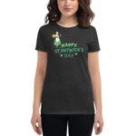 A woman wears a dark T-shirt featuring a graphic of a girl in a green dress holding a gold pot with the text Happy St. Patrick's Day in green letters.