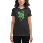 A woman stands wearing a dark t-shirt featuring stylized green text that reads "Real King" with a crown above and "Happy St. Patrick's Day" below in smaller font.