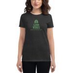 A person wears a dark gray t-shirt with green text and graphic  promoting festive sentiments for St. Patrick's Day with the phrases "GOOD VIBES" and "HAPPY ST.PATRICK'S DAY" on it.
