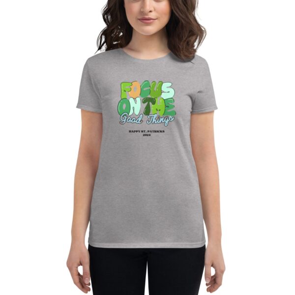 A woman is wearing a gray t-shirt featuring the text "FOCUS ON THE Good Things HAPPY ST. PATRICKS 2024" in colorful letters  suggesting a festive and positive theme.