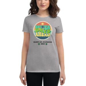 A woman wears a gray t-shirt featuring a circular graphic with the text "BETTER DAYS AHEAD" and "HAPPY ST. PATRICKS 2024 " surrounded by a sun and colorful stripes.