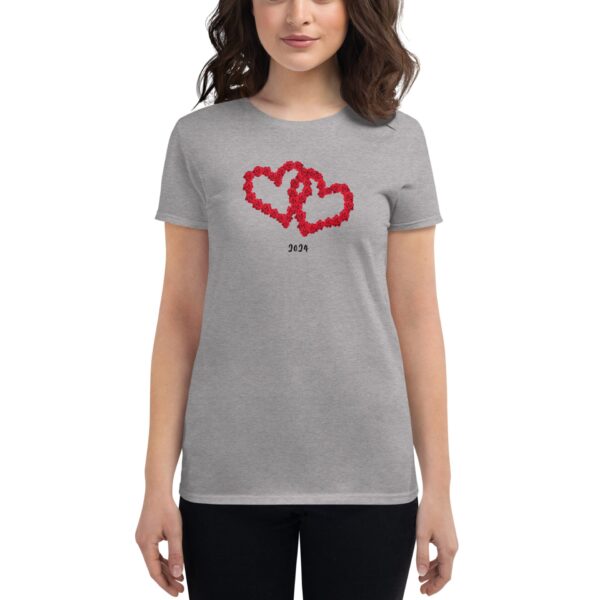 A woman wears a gray t-shirt adorned with two intertwined red hearts made of flowers and the year 2024 below them  standing against a plain background.