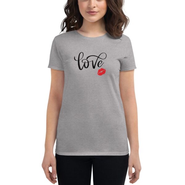 A woman stands wearing a gray t-shirt featuring the word love in stylish font alongside a red kiss mark printed on the front against a neutral background.