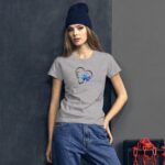 A young woman stands confidently  wearing a gray t-shirt with a heart design featuring the word love and colorful flowers  paired with loose jeans and a dark beanie against a dark wall.