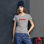 A young woman leans against a dark wall wearing a gray t-shirt with red hearts and the word LOVE printed on it paired with blue jeans and a dark beanie.