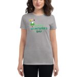 A woman wears a gray t-shirt featuring a character holding a mug and green decorations with the text HAPPY ST. PATRICK'S DAY  celebrating the holiday in a casual setting.
